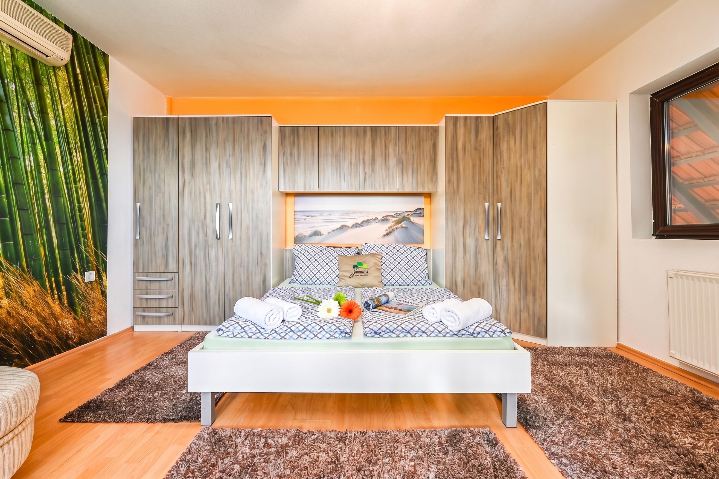 A modern bedroom with a bed, a wardrobe, and a large window.