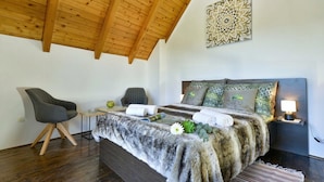 A bedroom with a wooden ceiling, a bed with a fur throw, two chairs, a bedside table, and a decorative wall piece. - Twin Oasis Retreat With Pool & Spa (Sveti Ivan Zelina)