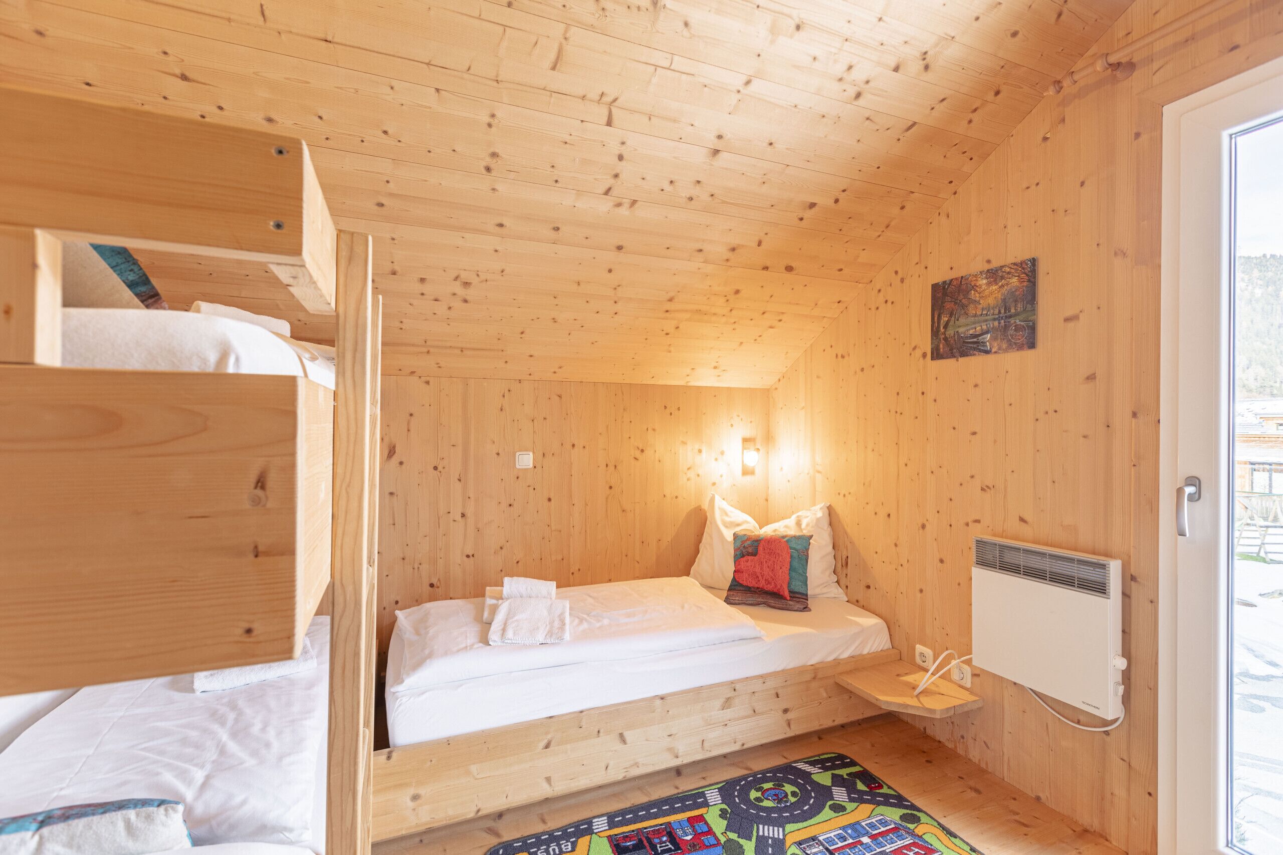 Ein Holzhüttenraum mit Etagenbetten, einem kleinen Nachttisch, einem Heizkörper und einem Fenster.