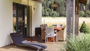 A wooden deck with a table and chairs, a lounge chair, and a hanging light fixture. - Chalet # 22 with 4 bedrooms & sauna (Murau)