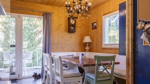 A wooden interior with a dining table, chairs, a chandelier, a clock, and a window with a view of greenery. - Chalet # 22 with 4 bedrooms & sauna (Murau)