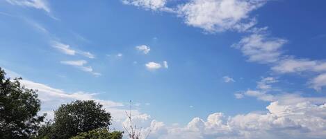 Une vue d’un paysage avec un ciel dégagé et quelques nuages épars, une ville visible au loin et un bâtiment doté d’un toit en pente.