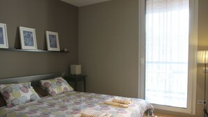 Une chambre à coucher avec un lit, des oreillers, une table de chevet, une lampe et une fenêtre avec des stores.