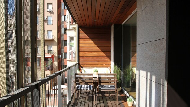 Un balcon doté d’un plancher en bois, d’une rambarde en métal et d’un banc avec des coussins.