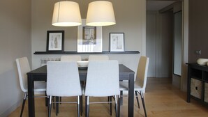 Un espace repas comprenant une table noire, quatre chaises grises et deux suspensions blanches.