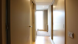 Un couloir avec une porte à gauche, un interrupteur à droite et une fenêtre au fond.