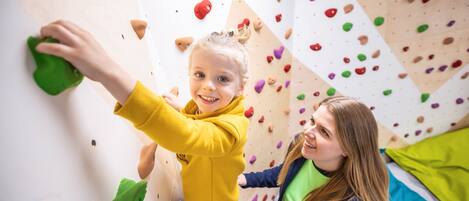 A child climbing a wall with colorful holds, and an adult standing beside them.