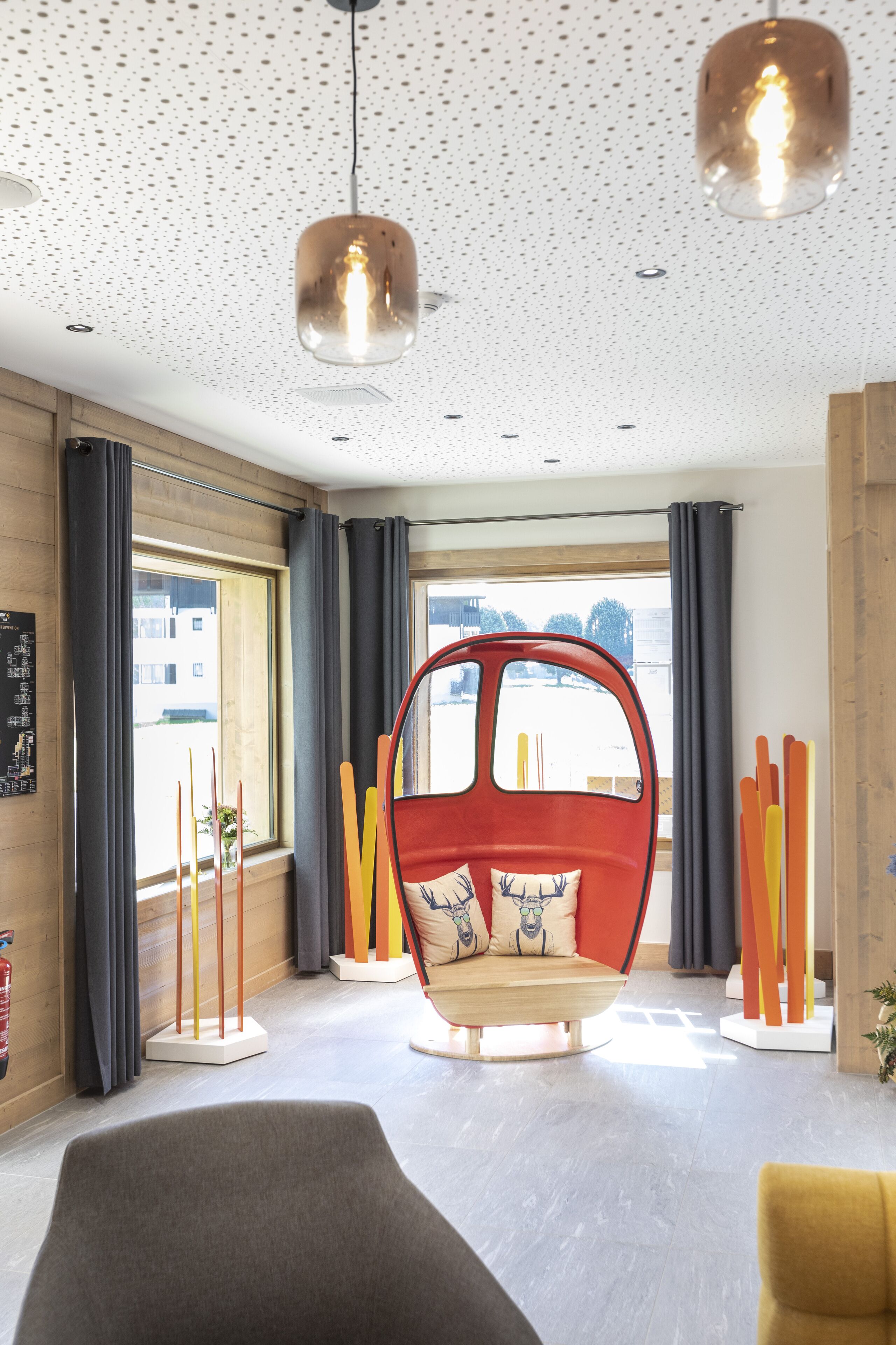 A modern interior with a unique red chair, large windows, and a ceiling with a speckled pattern.