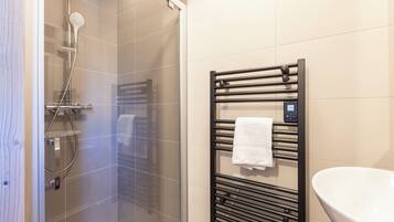 Un baño moderno con cabina de ducha de vidrio, un perchero negro con panel de control y un lavabo blanco.