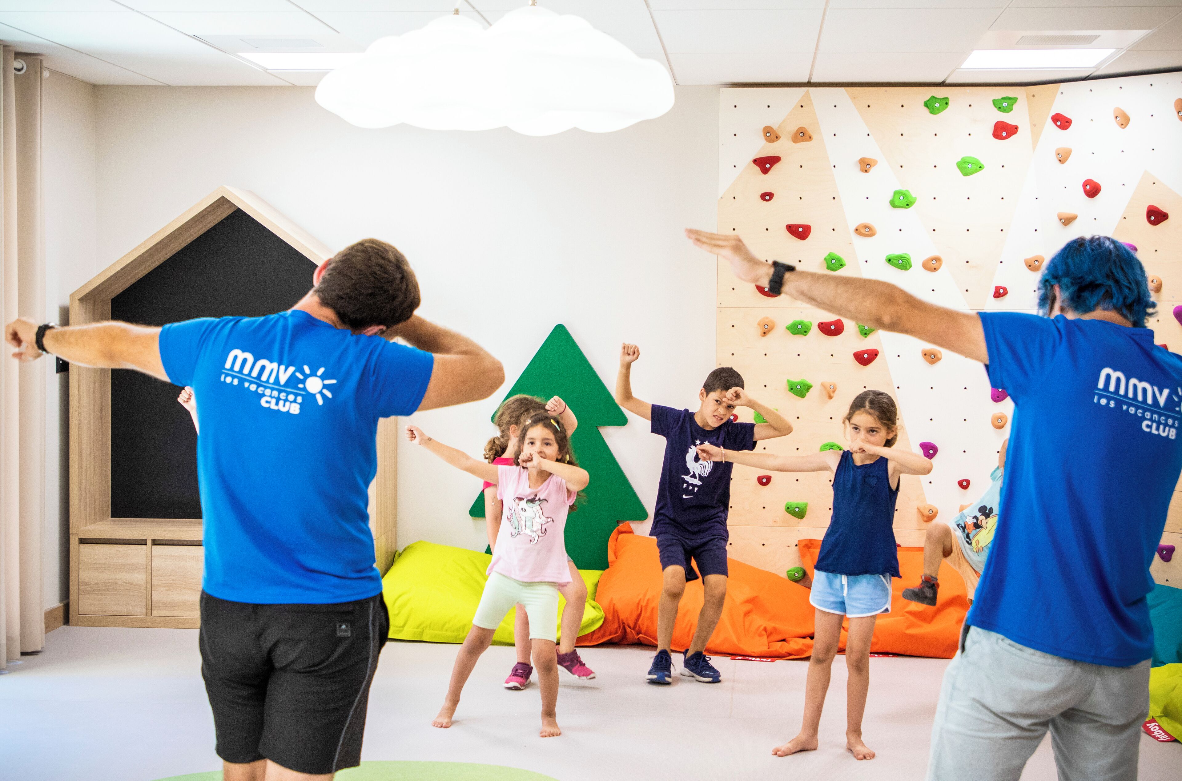 Un grupo de personas en una habitación con una pared de escalada y una casita de juegos de madera.