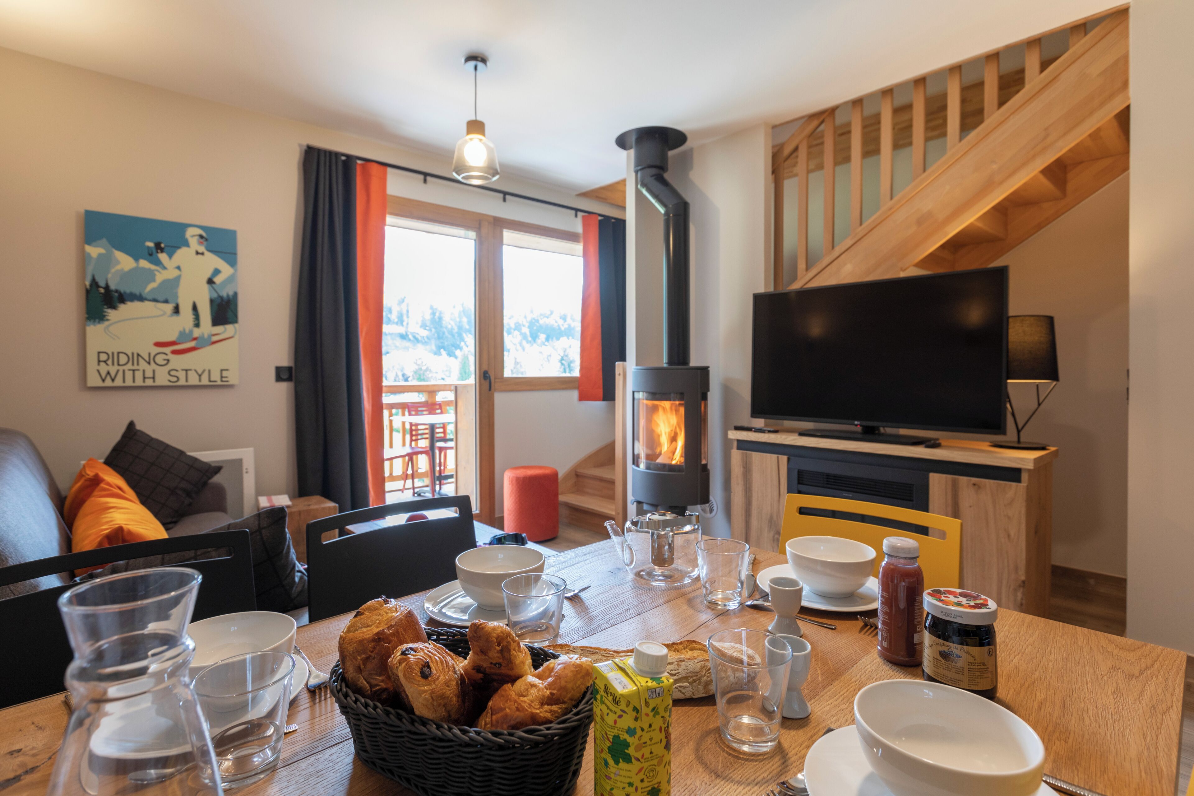Ein gemütliches Wohnzimmer mit Kamin, Fernseher und Essbereich mit gedecktem Tisch für das Frühstück.