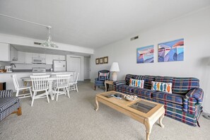 A living room with a plaid sofa, a coffee table, and a dining area with white chairs and a white table. - Two bedroom, two bath North Ocean City with indoor and outdoor pool! (Ocean City)
