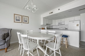 Un comedor con una mesa redonda y sillas, una cocina con armarios blancos y una araña.