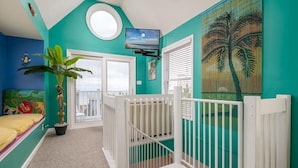 A room with teal walls, a large window, a round skylight, a white crib, and a potted plant.