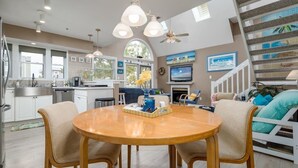 A modern kitchen with a dining area, large windows, and a staircase leading to a loft bedroom.