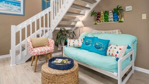 A living room with a staircase, a sofa, a chair, and a basket.