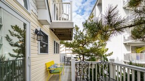 A balcony with a yellow bench, metal chairs, and a white railing.