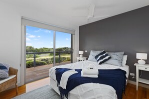 Een slaapkamer met een groot bed, een nachtkastje, een lamp en uitzicht op een groen landschap door een schuifdeur.