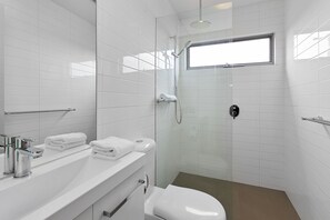 Een moderne badkamer met een douchecabine van glas, een toilet en een wastafel met een handdoekhouder.