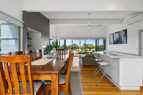 A modern kitchen with a dining area, large windows, and a view of the outdoors. - Great Ocean Road Lodge (Skenes Creek)