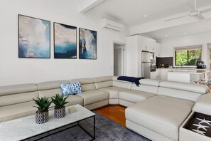 Una sala de estar moderna con un sofá modular, una mesa de centro y una cocina visible a través de un umbral abierto.