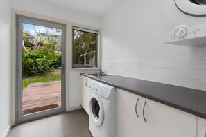 A laundry room with a washing machine, a sink, and a window overlooking a garden. - Great Ocean Road Lodge (Skenes Creek)
