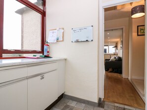 A kitchen area with a white countertop, a window with a red frame, a fire extinguisher, and a bulletin board with notices. - Steading Cottage (Kirriemuir)