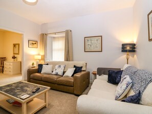 A living room with a brown sofa, a white sofa, a coffee table, a lamp, and a framed picture on the wall. - Steading Cottage (Kirriemuir)