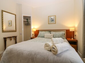 A neatly made bed with a white duvet, two rolled towels, and a wooden bedside table with a lamp. - Steading Cottage (Kirriemuir)