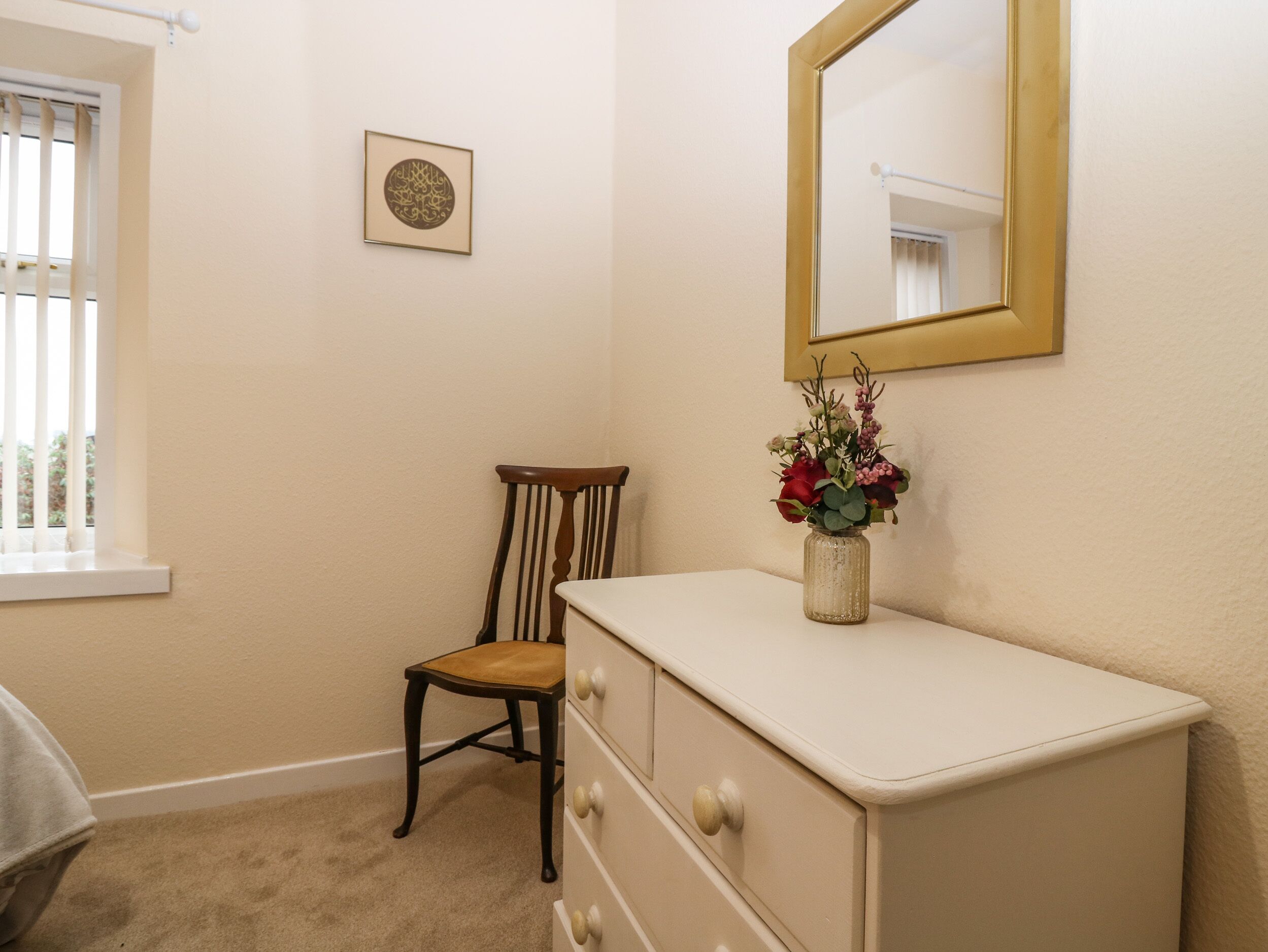 A bedroom with a dresser, a chair, a mirror, and a framed artwork on the wall.