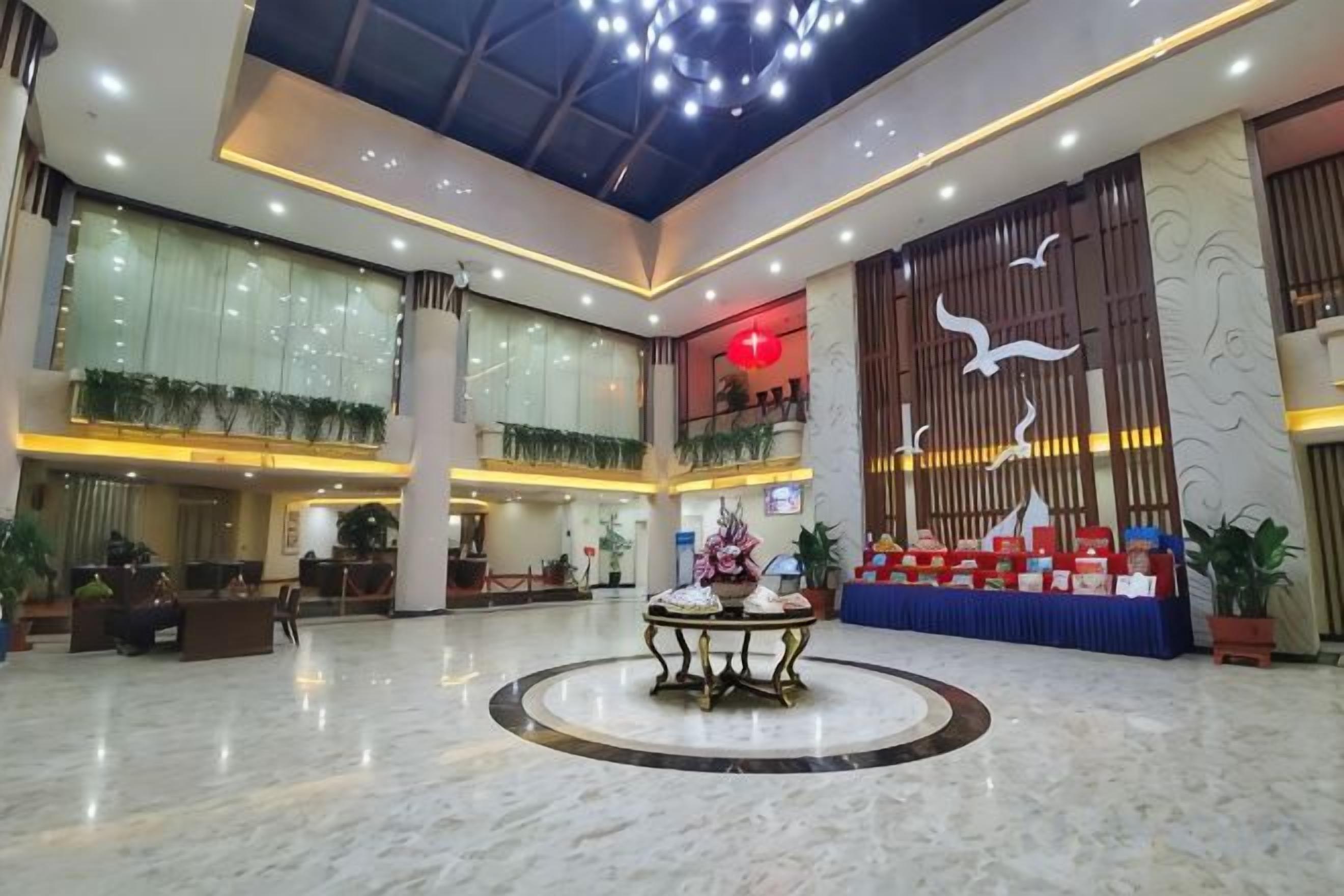 A spacious lobby with a central round table, a reception desk, and a large decorative wall.