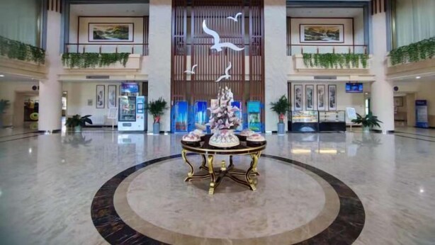 Um hall amplo com uma mesa decorativa central, obras de arte emolduradas nas paredes e plantas em vasos.