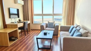Quarto com piso de madeira, uma escrivaninha com cadeira, sofá e televisão na parede.