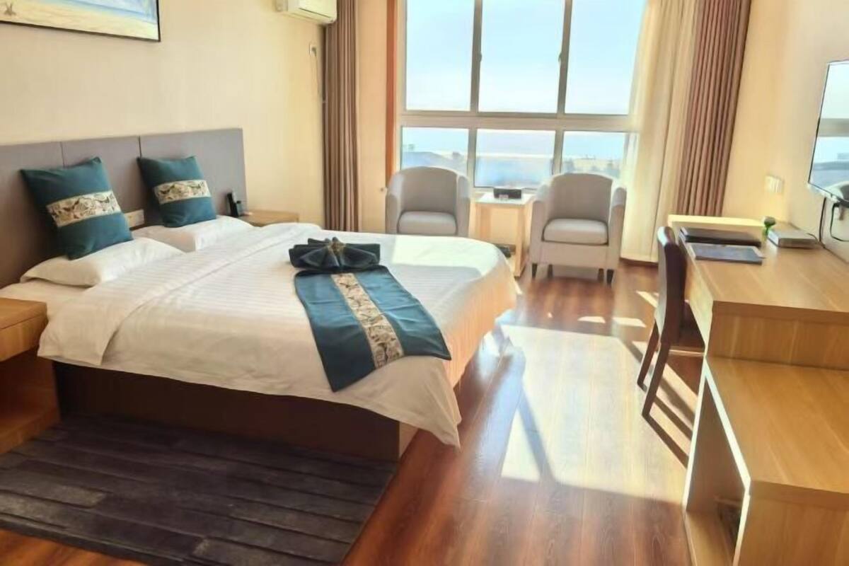 Ein Hotelzimmer mit einem großen Bett, zwei Sesseln, einem Schreibtisch und Meerblick.
