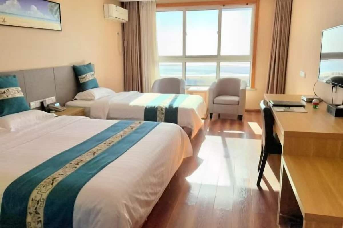 Ein Hotelzimmer mit zwei Betten, einem Schreibtisch, einem Stuhl, einem Fenster mit Aussicht und einem Gemälde an der Wand.