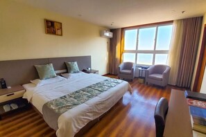 Une chambre d’hôtel avec un grand lit, un bureau, deux chaises, une petite table et une fenêtre avec des rideaux.
