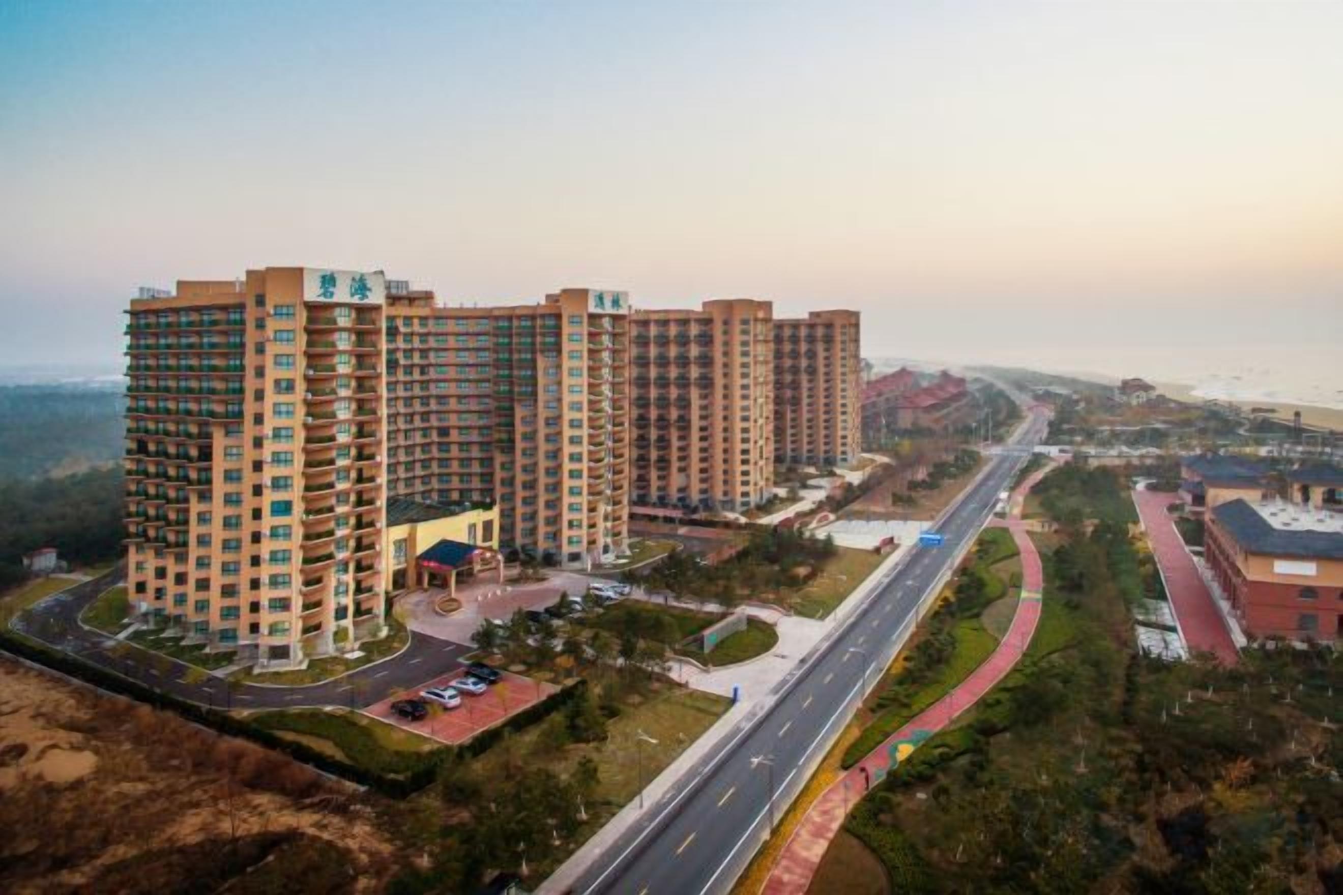 A high-rise residential building complex with multiple floors, a central courtyard, and a road running alongside.