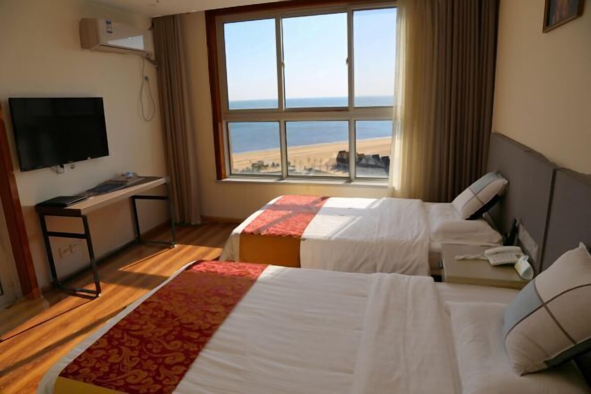 Une chambre d’hôtel avec deux lits, un bureau, une télévision et une grande fenêtre donnant sur la plage.