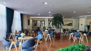 Um hall de hotel com mesas redondas e cadeiras azuis, uma grande planta de interior e uma área de bar ao fundo.