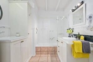 Bathroom features a white vanity with sink and mirror, glass shower enclosure, and hairdryer.