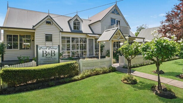 Ein zweigeschossiges Haus mit einem Schild, das 'Creek Cottage B&B' und '3 luxuriöse Suiten' bewirbt.