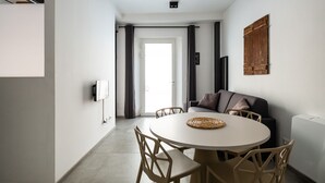 A compact living space with a round dining table, beige chairs, a sofa, and a wooden ceiling beam. - San Michele Apartments - Lapis by Wonderful Italy (Bologna)