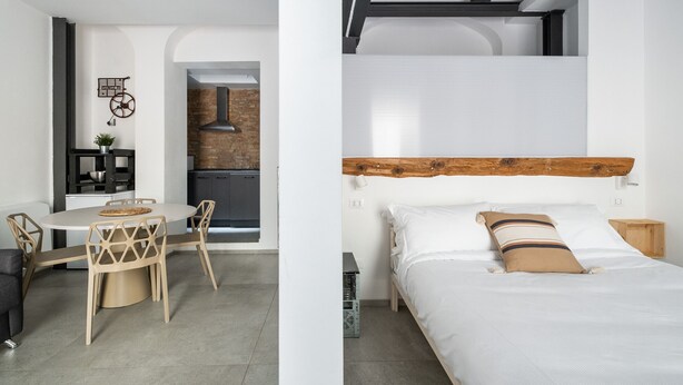 A modern room with a round dining table, chairs, a bed with a wooden headboard, and a small wooden nightstand. - San Michele Apartments - Lapis by Wonderful Italy (Bologna)