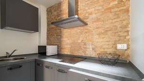 A kitchen with a brick wall, stainless steel cabinets, a microwave, and a modern range hood. - San Michele Apartments - Lapis by Wonderful Italy (Bologna)