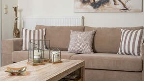 Olohuone, jossa on beigenvärinen sohva, raidallisia koristetyynyjä, lasinen kynttilänjalka ja puinen sohvapöytä.