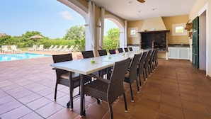 A covered outdoor dining area with a pool view, a brick fireplace, and a ceiling fan. - Fandango  Stunning Finca near Cala Dor with Large Garden and Private Pool, A/C (balearic islands)