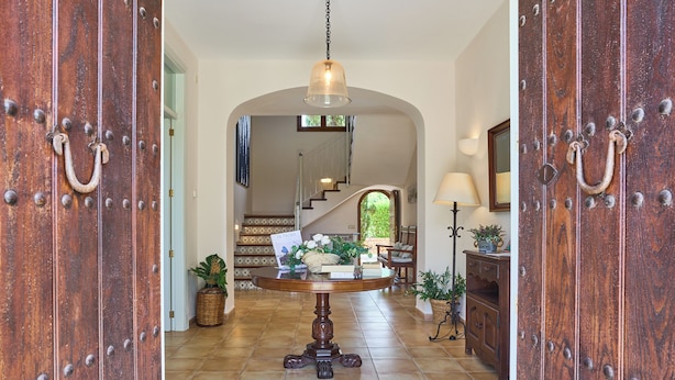 A grand entrance with a wooden door, a round table with a lamp, and a staircase leading to an upper level. - Fandango  Stunning Finca near Cala Dor with Large Garden and Private Pool, A/C (balearic islands)