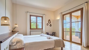 A hotel room with a bed, two bedside tables, a window with curtains, a view of the outdoors, and a balcony with a chair. - Fandango  Stunning Finca near Cala Dor with Large Garden and Private Pool, A/C (balearic islands)