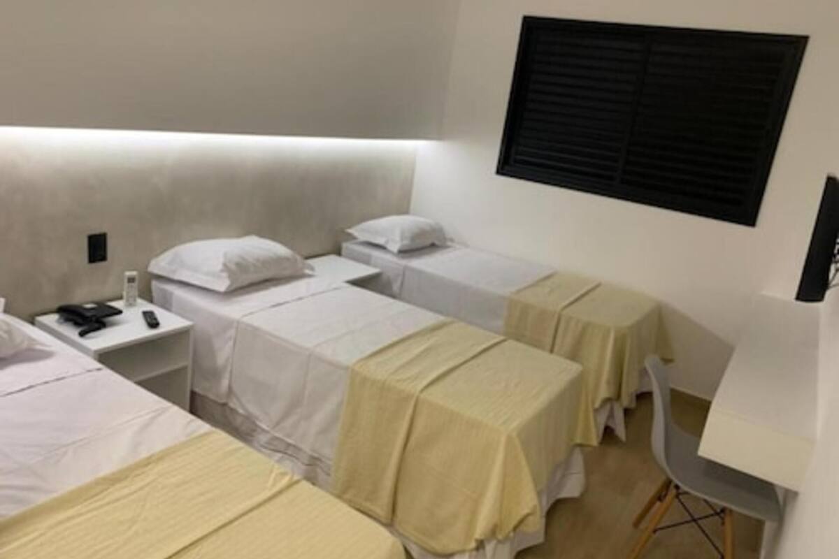 Habitación de hotel con dos camas individuales, un escritorio, una silla y un ventanal con persianas.
