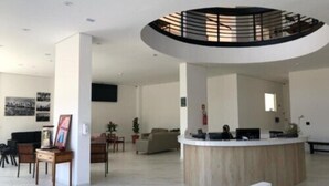 Um hall amplo com uma receção central, teto alto e uma clarabóia circular.